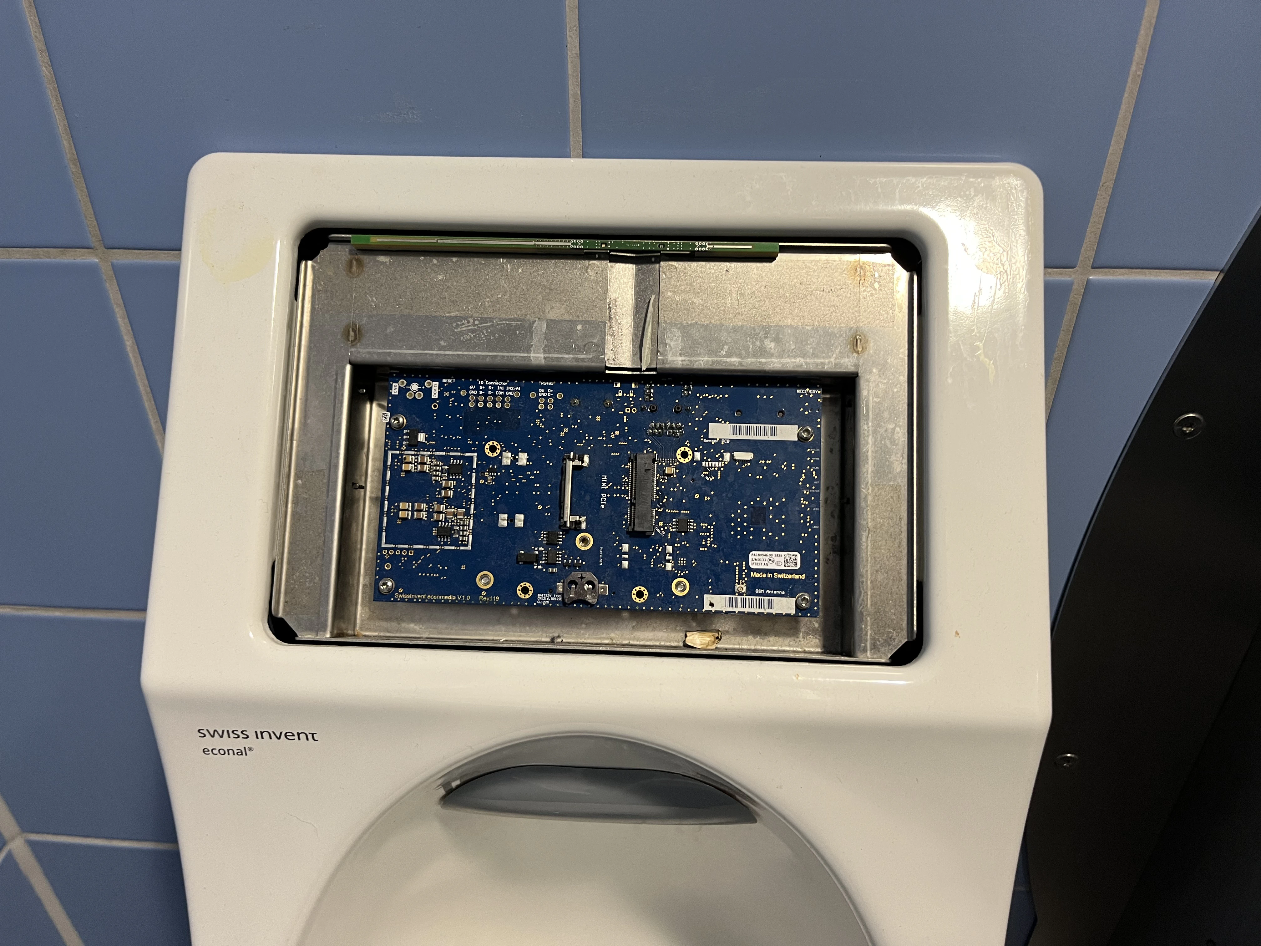 Urinal showing an exposed embedded board, the display seems to be missing